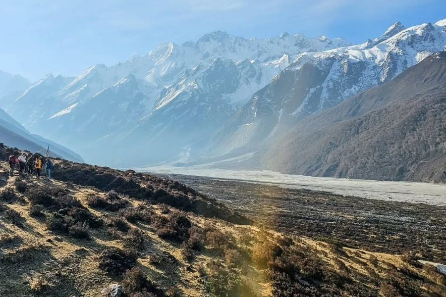 Trekkers hiking on Langtang Valley trail in autumn with glacial valley and snow-capped Himalayan peaks in background